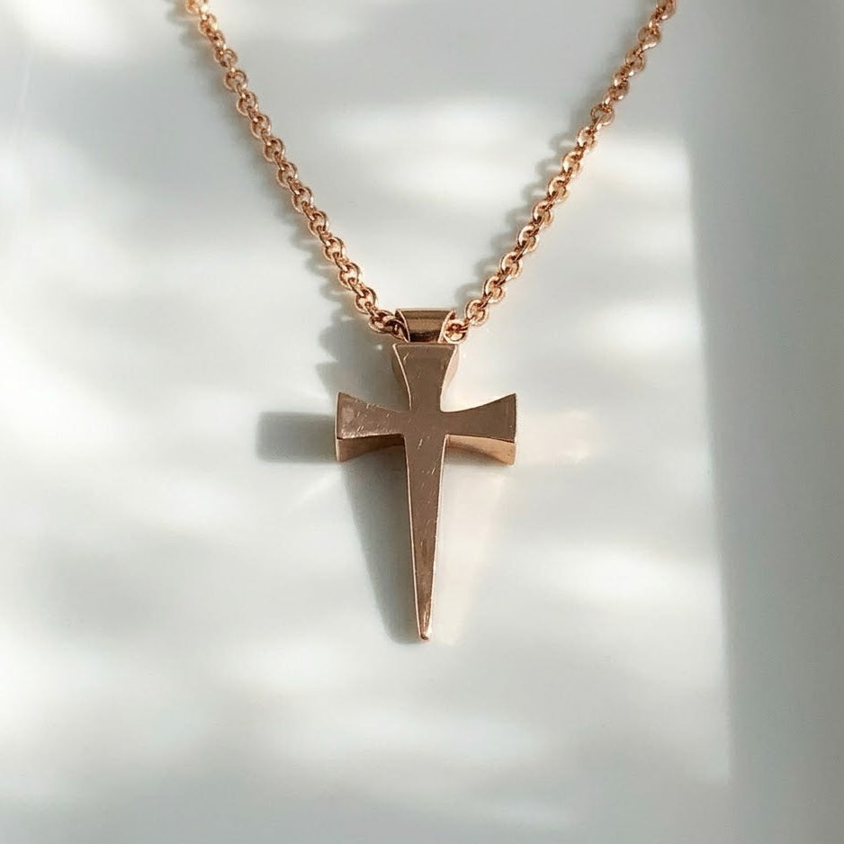 Rose gold cross necklace on a white background
