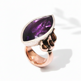 A rose gold ring with a large marquise cut purple amethyst stone, featuring a traditional lotus design.