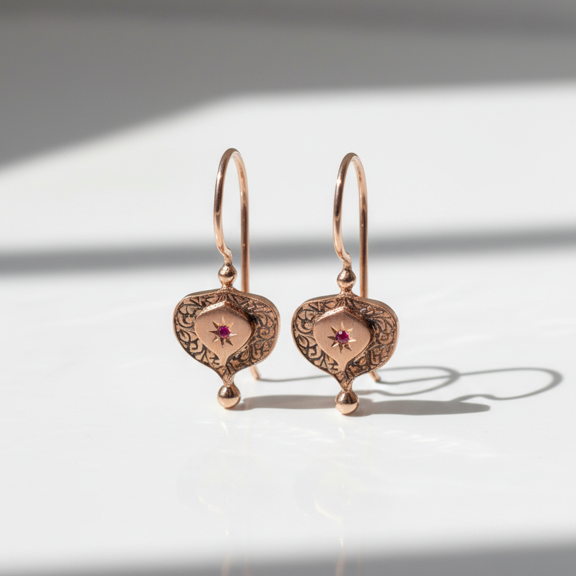 Pair of rose gold earrings with intricate designs on a light background