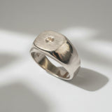 A solid 9-karat white gold signet-style ring with a matte emery finished face and a high polished body, set with a natural diamond.