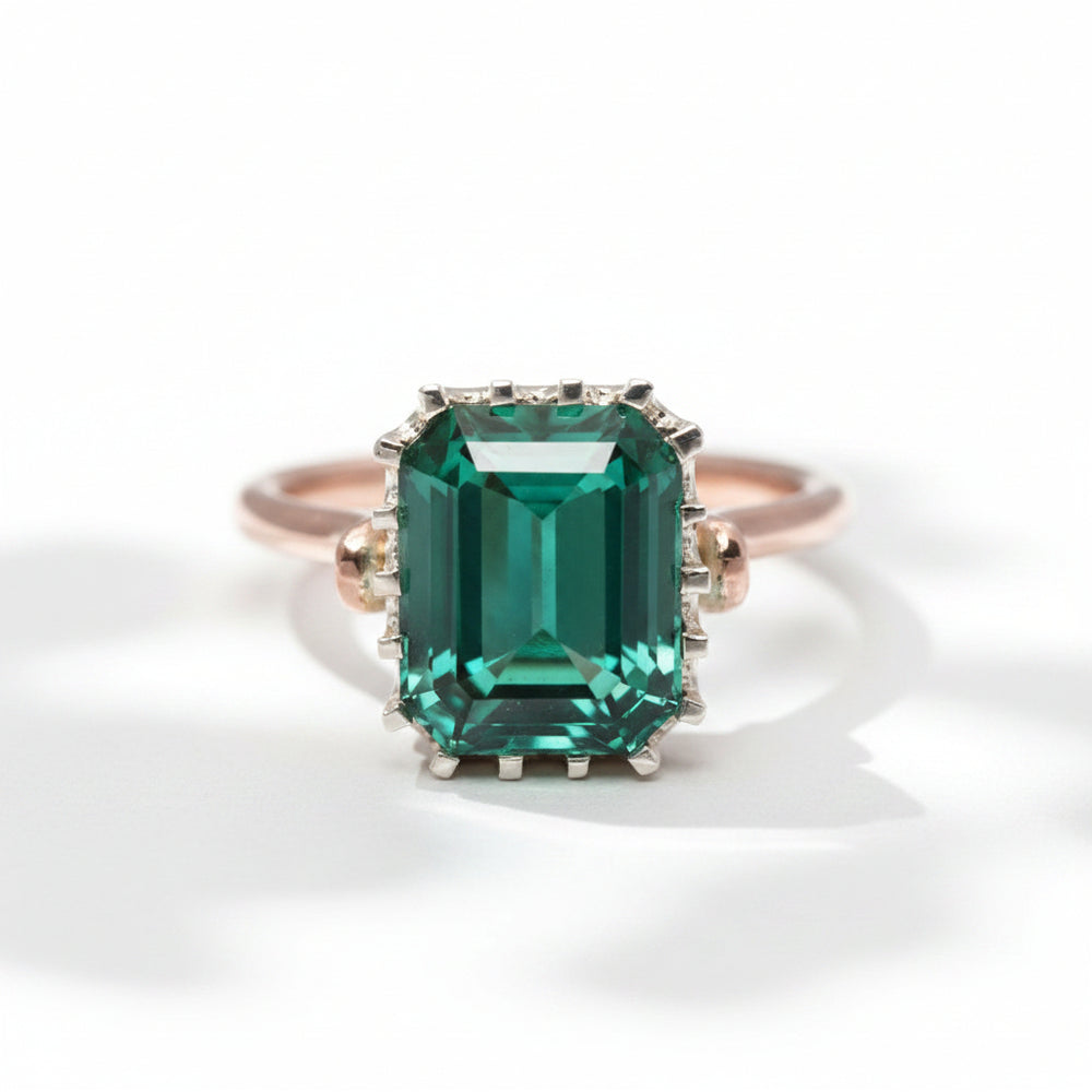 An emerald-cut tourmaline ring with a rose gold band and a white gold bezel, set with smaller tourmalines around the main stone.