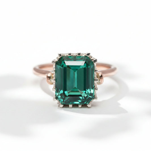 An emerald-cut tourmaline ring with a rose gold band and a white gold bezel, set with smaller tourmalines around the main stone.