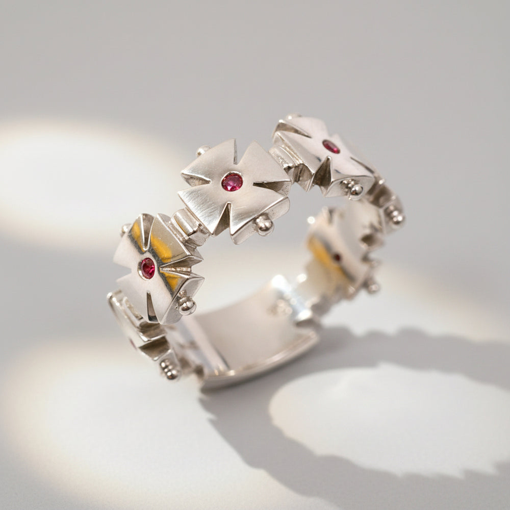 A white gold ring featuring a geometric cross design with a central ruby and smaller rubies on the arms of the cross.