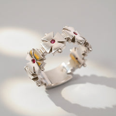 A white gold ring featuring a geometric cross design with a central ruby and smaller rubies on the arms of the cross.