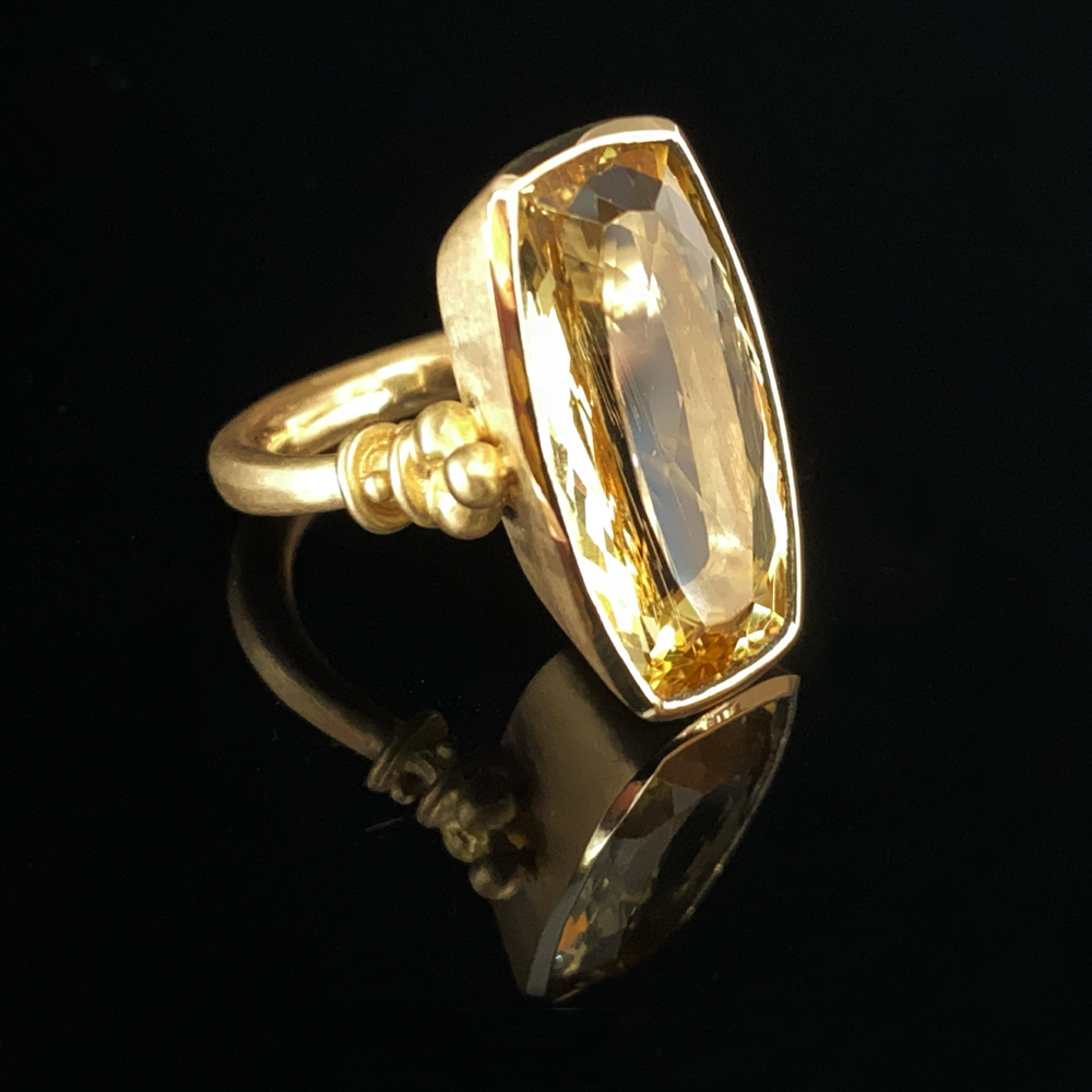 A golden ring with a large natural beryl stone set in a matte solid 18-karat gold band, featuring an Etruscan weighted shank design with a unique ball collar and triad motif.