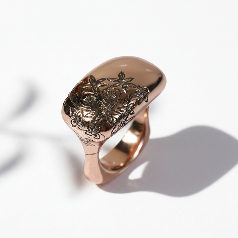A rose gold ring with a nature-inspired floral motif hand-carved on the top surface.