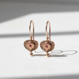 Pair of rose gold earrings with intricate designs on a light background