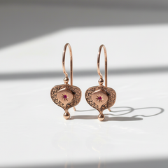 Pair of rose gold earrings with intricate designs on a light background