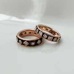 Two rose gold bands featuring geometric patterned detailing and embedded with round and princess cut diamonds set against a blackened background.