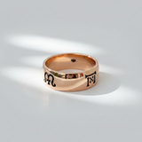 A handcrafted rose gold band ring with engraved symbols representing the four seasons on its surface.