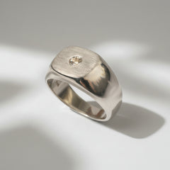 A solid 9-karat white gold signet-style ring with a matte emery finished face and a high polished body, set with a natural diamond.