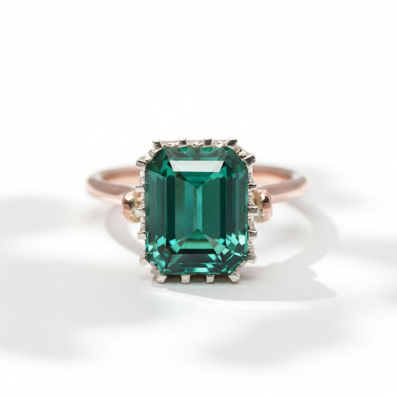 An emerald-cut tourmaline ring with a rose gold band and a white gold bezel, set with smaller tourmalines around the main stone.