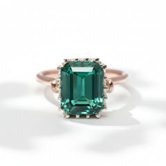 An emerald-cut tourmaline ring with a rose gold band and a white gold bezel, set with smaller tourmalines around the main stone.