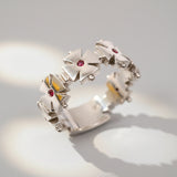 A white gold ring featuring a geometric cross design with a central ruby and smaller rubies on the arms of the cross.