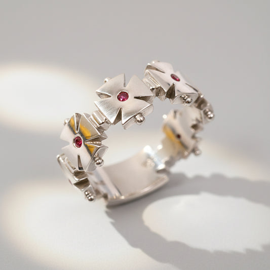 A white gold ring featuring a geometric cross design with a central ruby and smaller rubies on the arms of the cross.