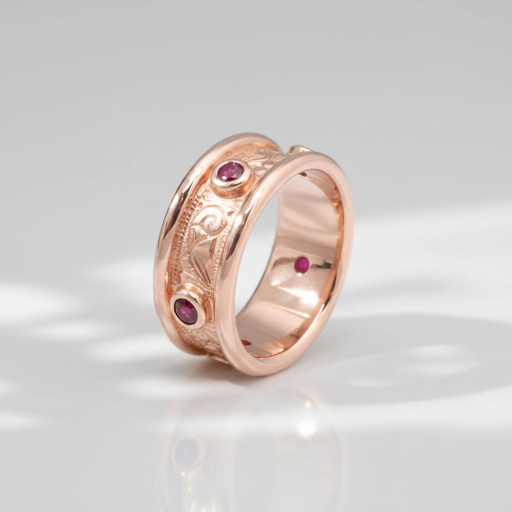 A rose gold band ring with hand engraved scrollwork and multiple small red gemstones set into the band.