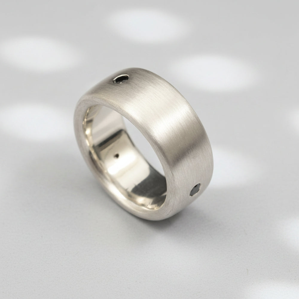 A matte-finished white gold ring with three natural black diamonds set in a row.
