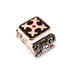 A handcrafted sterling silver ring with a 9-karat rose gold cross and a natural ruby in the center, featuring intricate detailing and a polished finish.